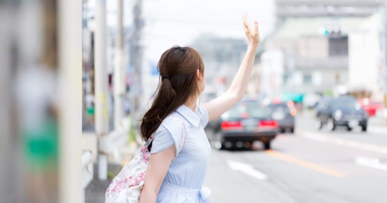 手を上げてタクシーを止めようとする女性