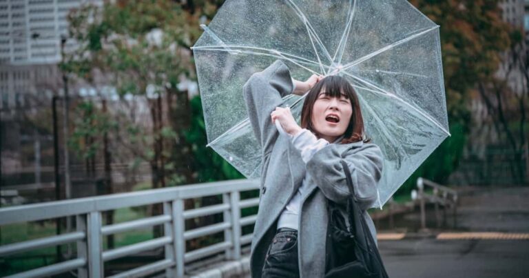 風に飛ばされそうな傘を持つ女性